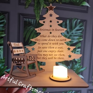 Könnte beinhalten: Weihnachtsdekoration aus Holz mit einem Baum mit Sternaussparungen und einem Schaukelstuhl. Der Baum hat einen eingravierten Text über Weihnachten im Himmel. Auf der Basis befindet sich eine kleine Kerze. Das Wort "Dad" steht auf dem Stuhl.