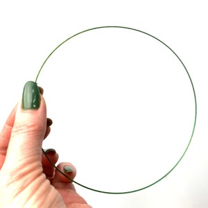 Può includere: Un cerchio di filo verde, tenuto in una mano con smalto verde.