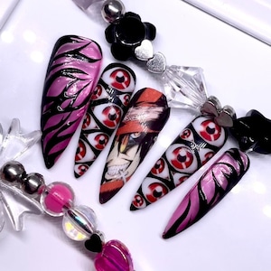 Peut inclure: Ensemble d'ongles artificiels avec des motifs roses et noirs. Certains ongles présentent un motif répété d'yeux rouges, tandis que d'autres présentent un personnage d'anime avec des yeux rouges et un chapeau rouge.