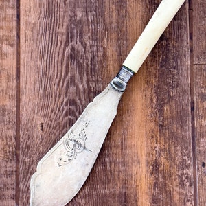 May include: A vintage silver butter knife with a bone handle. The knife has an ornate design on the blade and is in good condition.