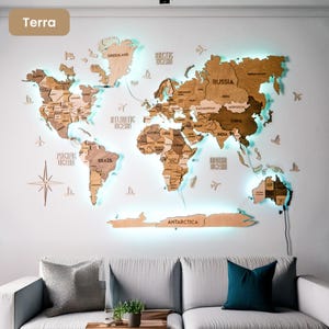 Op de afbeelding: Een grote houten wereldkaart als wanddecoratie in verschillende bruintinten met gegraveerde landnamen en achtergrondverlichting die een zachte blauwe gloed werpt. Inclusief decoratieve houten iconen van vliegtuigen, schepen en een windroos.