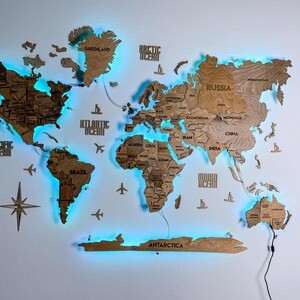 May include: A multi-layered wooden world map wall art piece featuring engraved country names, continents, and oceans. The map includes decorative wooden airplanes, ships, and a compass rose, illuminated from behind by a bright blue LED light.