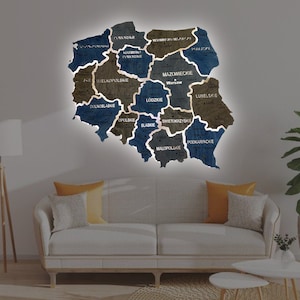 May include: A wooden map of Poland with each region outlined in white and labeled with the region's name in Polish. The map is painted in shades of blue and brown and has a light blue background. The map is hanging on a wall in a room with a couch and a lamp.