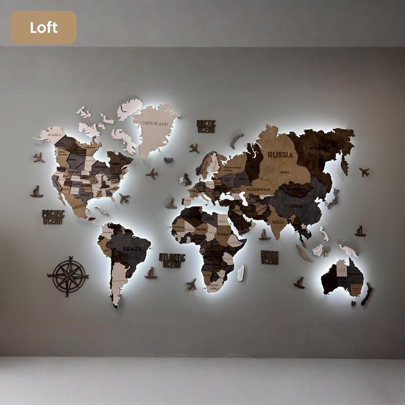 Op de afbeelding: Een grote houten wereldkaart als wanddecoratie met continenten in verschillende bruin- en grijstinten en ge&iuml;ntegreerde led-achtergrondverlichting. De kaart bevat uitgesneden landnamen, een kompasroos en kleine decoratieve houten vliegtuigen en schepen.
