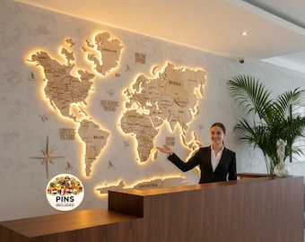 Könnte beinhalten: Eine Weltkarte aus Holz mit beleuchteten Rändern ist an einer Wand befestigt. Die Karte wird von einer Windrose und dem Text "PINS INCLUDED" auf einem Aufkleber begleitet. Eine Person steht hinter einem Empfangstresen aus Holz.