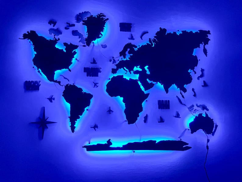 Op de afbeelding: Een donkergekleurde wereldkaart als wanddecoratie met een levendige blauwe LED-achtergrondverlichting die de continenten verlicht. De kaart bevat kleine decoratieve iconen van vliegtuigen en schepen, samen met een kompasroos aan de linkerzijde.