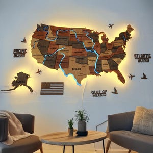May include: A wooden illuminated map of the United States, with each state individually cut and labeled. The map features blue LED lighting along the state borders and major rivers. Additional wooden cutouts include the words "PACIFIC OCEAN", "ATLANTIC OCEAN", "GULF OF MEXICO", and the state of Alaska.