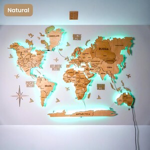 Op de afbeelding: Een houten wereldkaart als wanddecoratie met lasergesneden continenten en landen voorzien van gegraveerde labels. De kaart bevat decoratieve houten vliegtuigen en schepen, een windroos en een heldere groene LED-achtergrondverlichting.