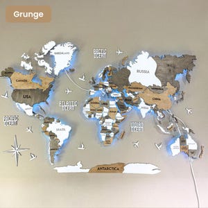 Op de afbeelding: Een meerlaagse houten wereldkaart als wanddecoratie met een mix van lichte en donkere houttinten en witte accenten. De kaart is voorzien van led-achtergrondverlichting, uitgesneden landnamen en decoratieve houten iconen van vliegtuigen.