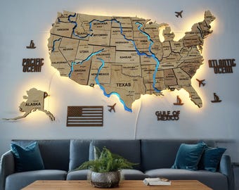 May include: A wooden map of the United States with illuminated blue rivers and state outlines. The map includes Alaska and is surrounded by wooden cutouts of airplanes, boats, and the words "PACIFIC OCEAN", "ATLANTIC OCEAN", and "GULF OF MEXICO".