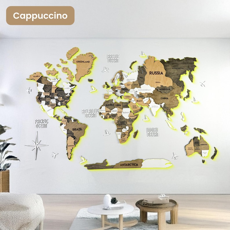 Op de afbeelding: Een grote houten wereldkaart als wanddecoratie in bruin- en beigetinten met verlichte randen. De kaart toont gelabelde continenten, landen en oceanen, geaccentueerd door kleine houten uitsparingen van vliegtuigen en zeilboten op de muur.