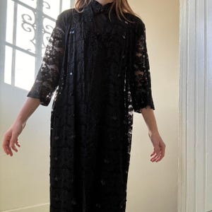 May include: A long, black lace dress with three-quarter sleeves and a matching long jacket. The dress and jacket are adorned with small, dark sequins. The outfit is suitable for formal occasions.