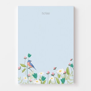 May include: A light blue notepad with the word "notes" printed at the top. The notepad has a floral border with pink flowers, green leaves, and a blue bird.