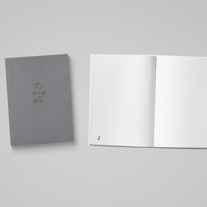 May include: A gray notebook with the text "the grey hats" on the cover. The notebook is open to a blank page with a grid pattern.