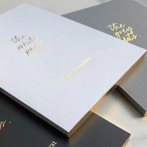 May include: Three notebooks with gold foil lettering. The white notebook says "the white pages" and "Dein Wunsch", the gray notebook says "the grey dots" and "Dein Wunsch", and the black notebook says "the black liner" and "Dein Wunsch".
