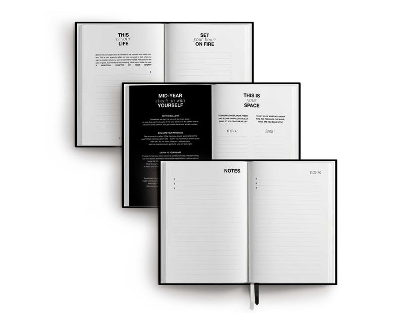 May include: Three open black hardcover journals with white pages are stacked on a white background. The top journal reads "THIS IS YOUR LIFE" and "SET YOUR HEART ON FIRE". The middle journal reads "MID-YEAR check-in with YOURSELF". The bottom journal reads "NOTES".