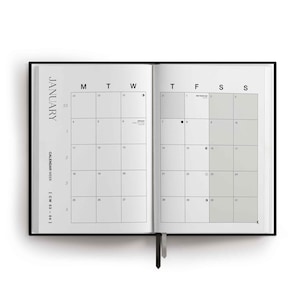 May include: An open planner showing a January calendar spread with white pages and black text. The left page displays the month name, calendar week, and dates. The right page features a grid with shaded weekend columns and lunar phase icons.