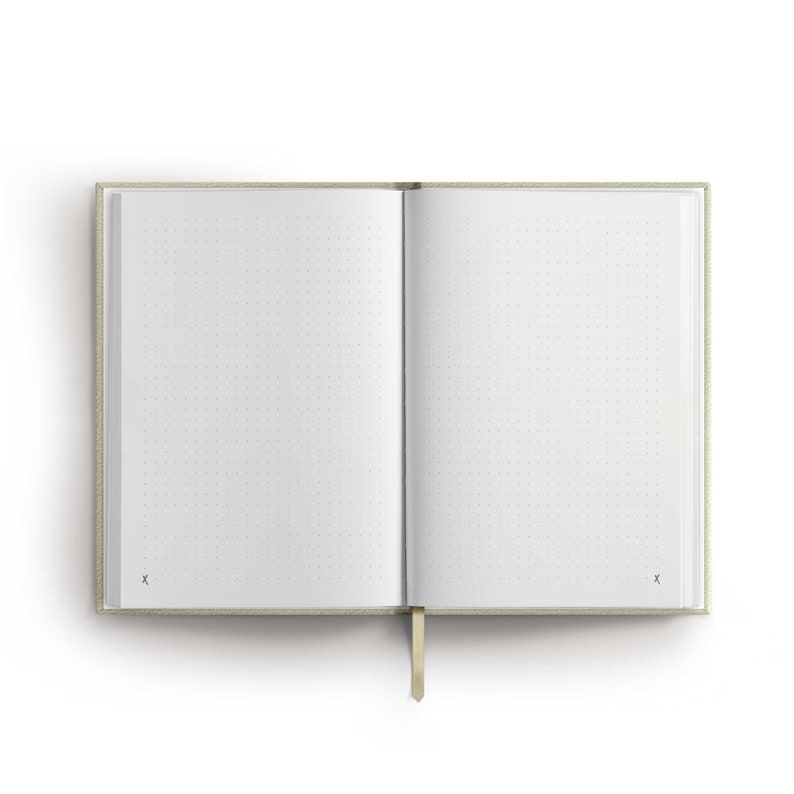 May include: A beige notebook with a dotted page layout and a gold ribbon bookmark. The notebook is open to a blank page.