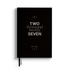 May include: A black rectangular planner with a textured cover featuring the text [ 2027 ] at the top, the words TWO thousand twenty SEVEN in the center, and the placeholder text Your Name followed by three X characters at the bottom.