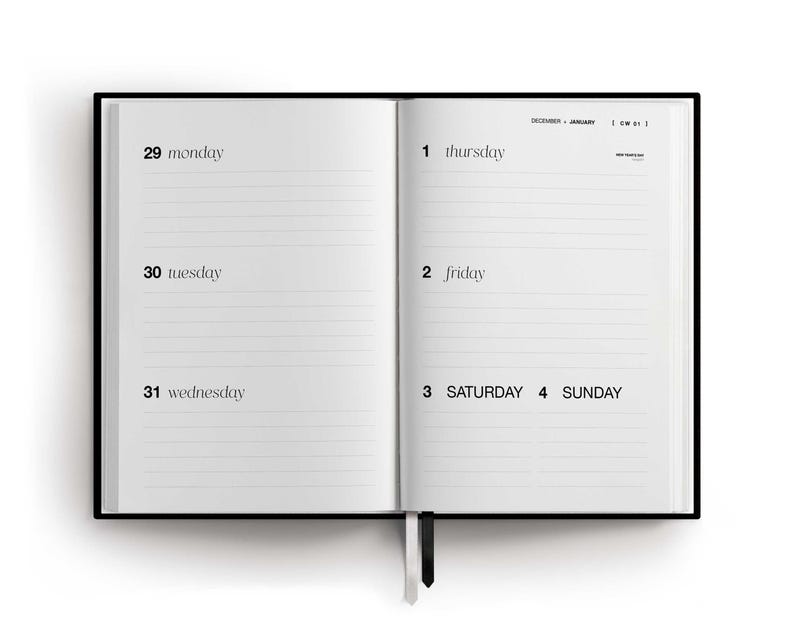 May include: Open black hardcover planner with lined pages. The left page shows Monday, Tuesday, and Wednesday dates. The right page shows Thursday, Friday, Saturday, and Sunday dates. A black ribbon bookmark is visible.