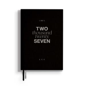 May include: A black planner with the text 2027 in brackets at the top, the words TWO thousand twenty SEVEN in the center, and three X symbols at the bottom. The cover has a textured finish and two thin ribbon bookmarks extending from the bottom edge.