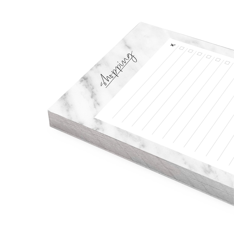 May include: A white notepad with a marble pattern and the word "Shopping" written in black cursive. The notepad has a checklist with checkboxes and lined paper for writing.
