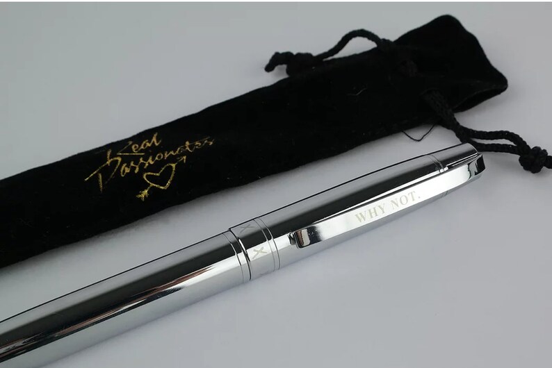 May include: A silver pen with the words "WHY NOT." engraved on the side. The pen comes with a black velvet pouch with the words "Real Passionistas" and a heart design in gold lettering.