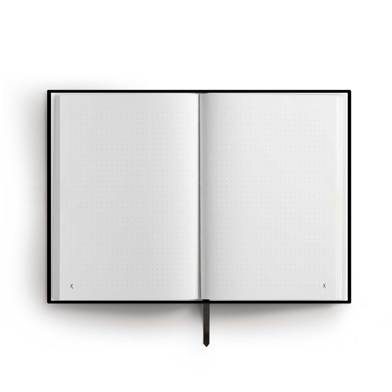 May include: A black hardcover notebook with a black ribbon bookmark. The notebook is open to a blank page with a dotted grid pattern.
