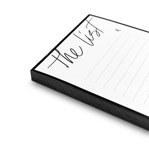 May include: A white notepad with a black border and the text "The List" written in black cursive. The notepad has lined paper and a check box at the top right corner.