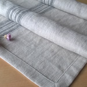 May include: A gray linen table runner with black stripes. The runner is folded and has a frayed edge. Dried flowers are on top of the runner.