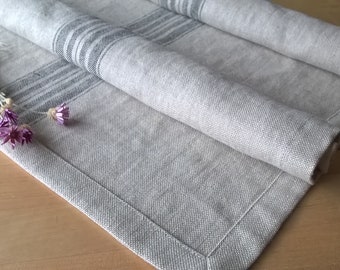 May include: A gray linen table runner with black stripes. The runner is folded and has a frayed edge. Dried flowers are on top of the runner.