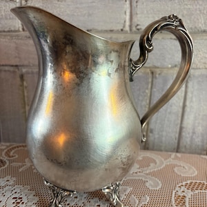 May include: A white ceramic mug with a black handle and the text "But First, Coffee" in a handwritten style. The mug is on a white surface. The mug is approximately 4 inches tall.