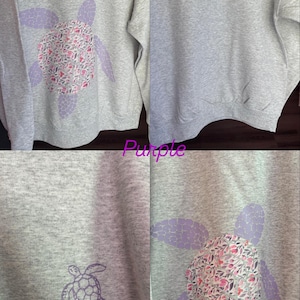 Puede incluir: Sudadera gris con un dise&ntilde;o de tortuga morada. El caparaz&oacute;n de la tortuga tiene un estampado floral en rosa, rojo y blanco. Un dise&ntilde;o de tortuga m&aacute;s peque&ntilde;o est&aacute; en el pecho izquierdo. La palabra "Purple" est&aacute; escrita en cursiva.