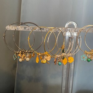 May include: A set of gold and silver hoop earrings with various charms, including leaves, flowers, and geometric shapes. The earrings are displayed on a clear plastic stand.