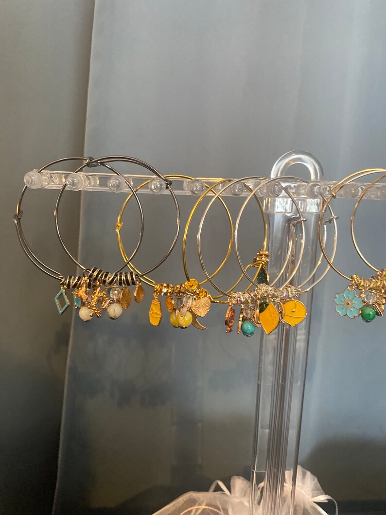 May include: A set of gold and silver hoop earrings with various charms, including leaves, flowers, and geometric shapes. The earrings are displayed on a clear plastic stand.