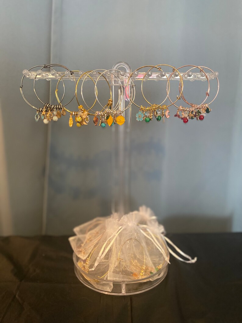 May include: A set of gold hoop earrings with various charms, including flowers, leaves, and beads. The earrings are displayed on a clear stand with a white organza bag.