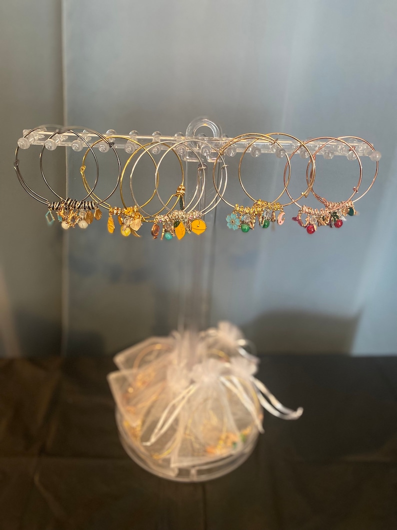 May include: A set of gold, silver, and rose gold bangle bracelets with charms. The charms are various colors and shapes, including flowers, leaves, and beads.