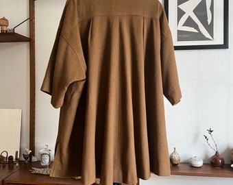 May include: A brown, oversized, collared shirt with a relaxed fit and short sleeves. The shirt is hanging on a black stand against a white wall.