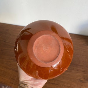 May include: A brown ceramic vase with a glazed finish. The vase has a rounded shape and a wide opening.