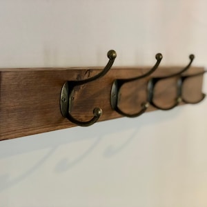 May include: A wooden coat rack with four hooks. The rack is stained a dark brown color and the hooks are a brass finish.