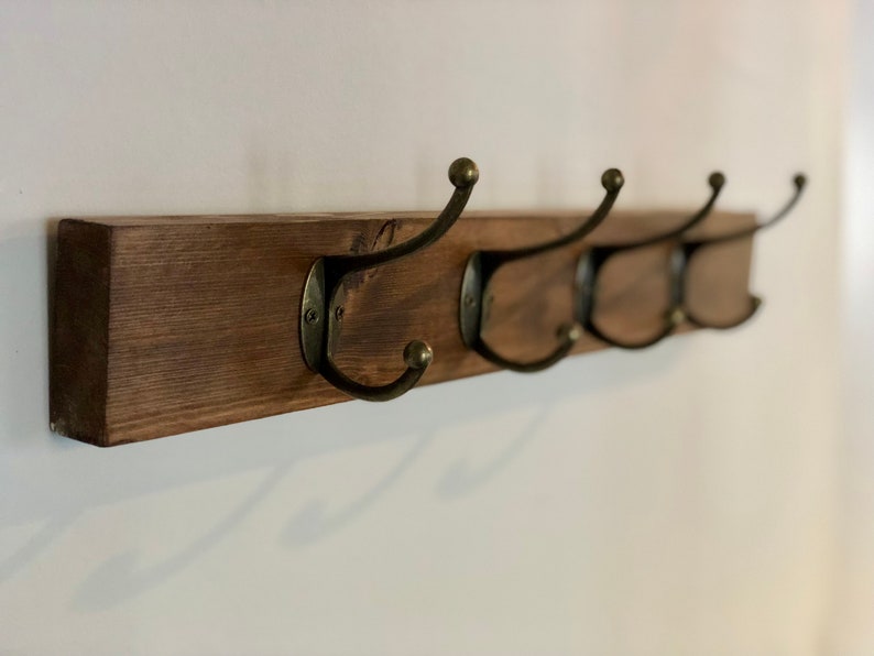 May include: A wooden coat rack with four hooks. The rack is stained a dark brown color and the hooks are a brass finish.