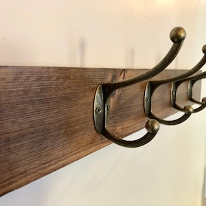 May include: A wooden wall-mounted coat rack with five antique brass hooks. The rack is stained a dark brown color.