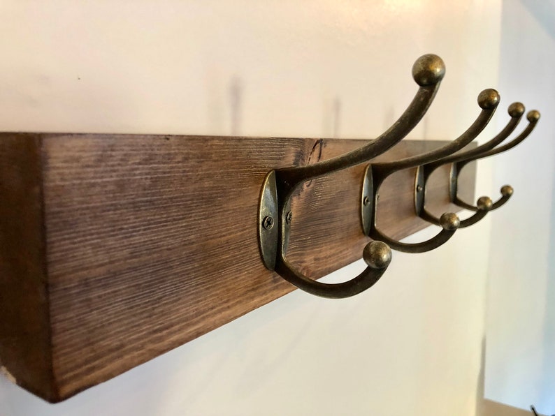 May include: A wooden wall-mounted coat rack with five antique brass hooks. The rack is stained a dark brown color.
