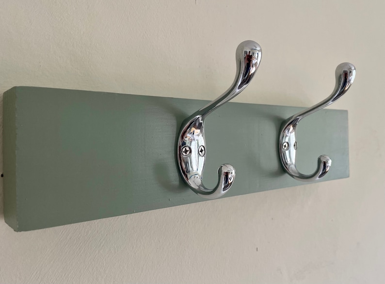K&ouml;nnte beinhalten: Ein hellgr&uuml;ner, an der Wand montierter Kleiderhaken mit zwei verchromten Haken.
