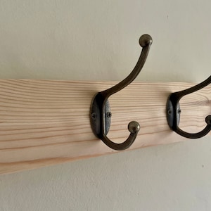 May include: A wooden coat rack with two antique brass hooks. The rack is made of natural wood with a light brown finish.