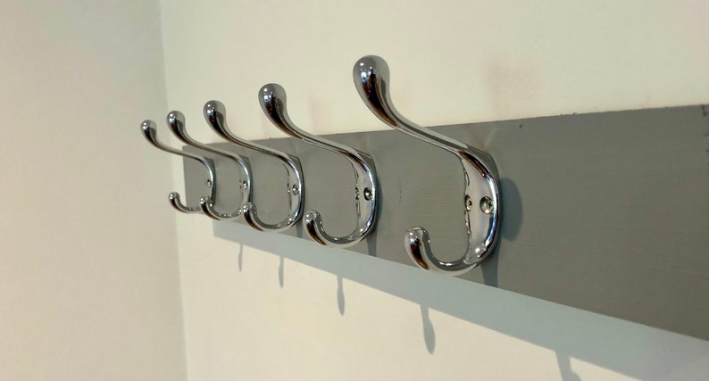 K&ouml;nnte beinhalten: Ein grauer, an der Wand montierter Kleiderst&auml;nder mit f&uuml;nf verchromten Haken.