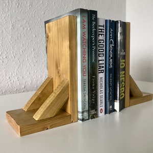 May include: Wooden bookends with a natural wood finish holding a stack of books with titles like "The Good Liar" and "I Am Watching You".