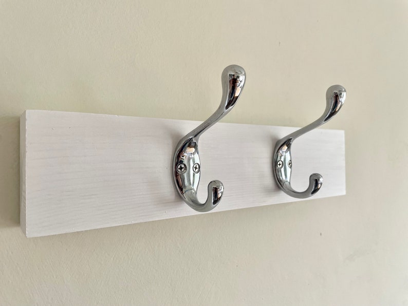 K&ouml;nnte beinhalten: Ein wei&szlig;er, an der Wand montierter Kleiderst&auml;nder mit zwei verchromten Haken.