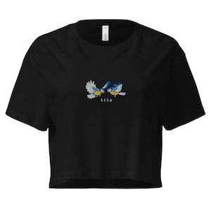 May include: Black cropped t-shirt with an embroidered image of two bluebirds facing each other. The text "tits" is embroidered below the birds.