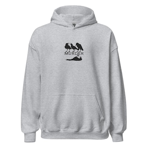 May include: A grey hoodie with a front pocket and a hood. The hoodie displays a black graphic of three crows above the word "MURDER" and a crow lying down.